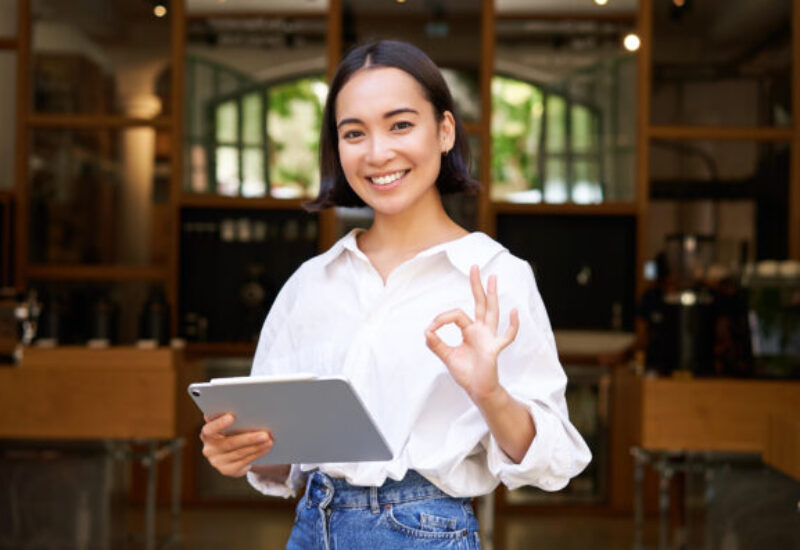 Young female entrepreneur, cafe manager standing with tablet and showing approval, recommending restaurant